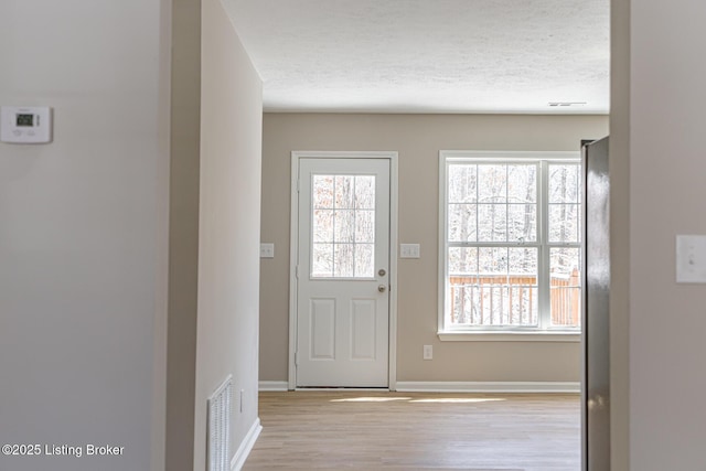 doorway to outside with a textured ceiling, baseboards, visible vents, and light wood-style floors