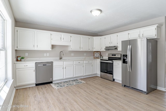 kitchen featuring stainless steel appliances, light countertops, under cabinet range hood, white cabinetry, and a sink