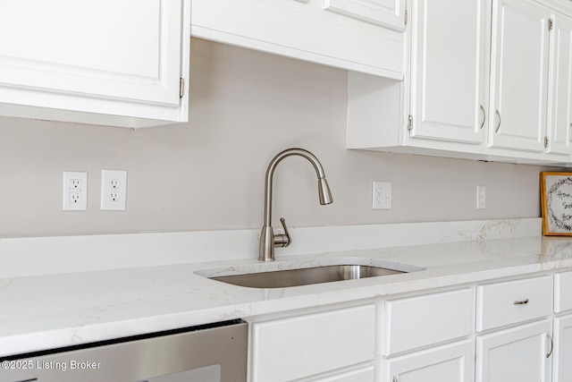 kitchen with light stone counters, white cabinets, a sink, and dishwashing machine