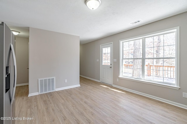 unfurnished living room featuring light wood finished floors, baseboards, visible vents, and a textured ceiling