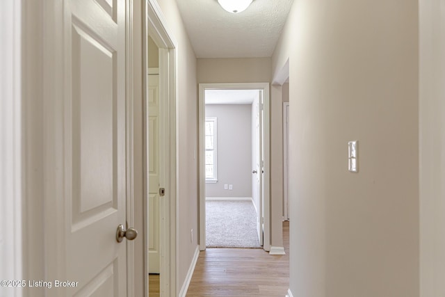 corridor featuring light wood-style flooring, baseboards, and a textured ceiling