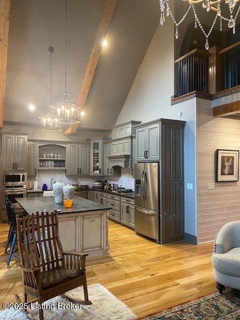 kitchen featuring beam ceiling, stainless steel appliances, dark countertops, gray cabinets, and glass insert cabinets