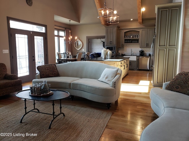 living area with a chandelier, french doors, high vaulted ceiling, and light wood-style flooring