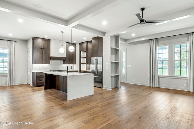 kitchen featuring dark brown cabinetry, high end refrigerator, light countertops, a center island with sink, and pendant lighting