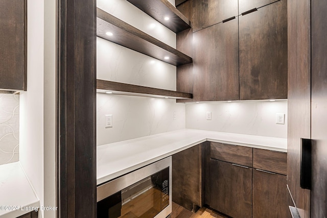 kitchen featuring modern cabinets, built in microwave, light countertops, dark brown cabinets, and open shelves