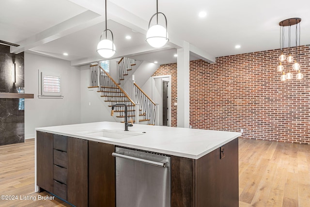 kitchen featuring pendant lighting, light countertops, stainless steel dishwasher, a sink, and brick wall