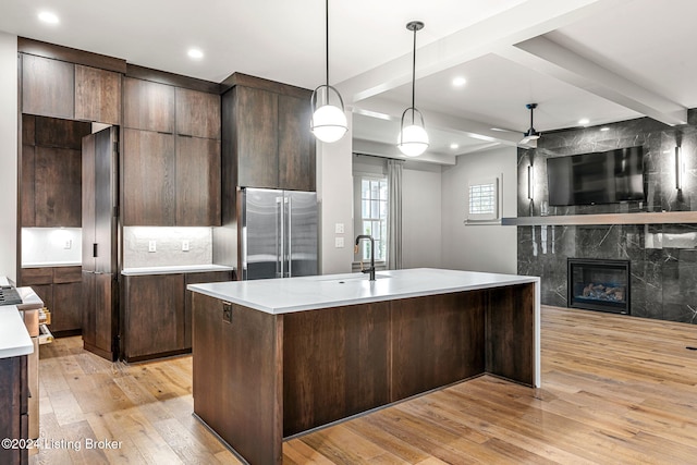 kitchen featuring high quality fridge, a sink, open floor plan, light countertops, and a center island with sink