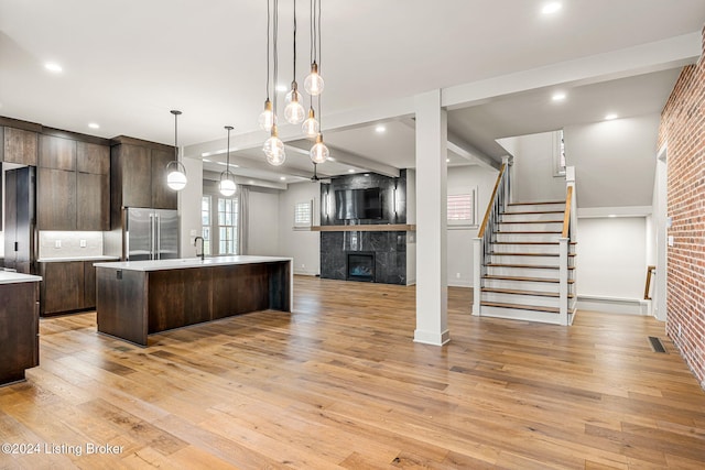 kitchen featuring a kitchen island with sink, high end refrigerator, open floor plan, light countertops, and decorative light fixtures