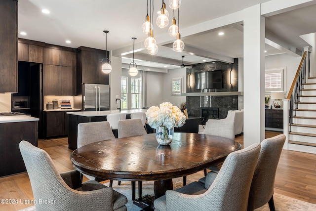 dining space with a high end fireplace, beamed ceiling, light wood finished floors, and stairs