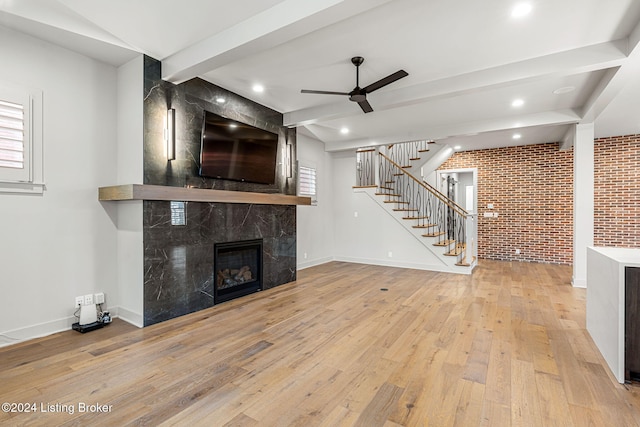 unfurnished living room with brick wall, stairway, light wood-style floors, a fireplace, and beam ceiling