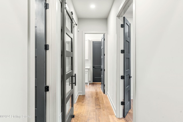 hallway featuring light wood finished floors, a barn door, and baseboards