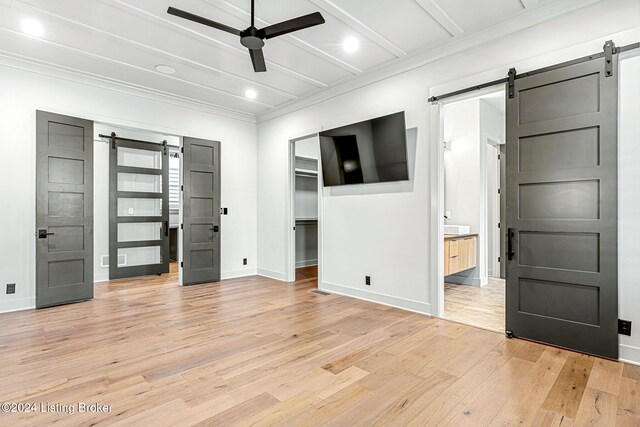 unfurnished bedroom with a walk in closet, crown molding, a barn door, light wood-type flooring, and baseboards