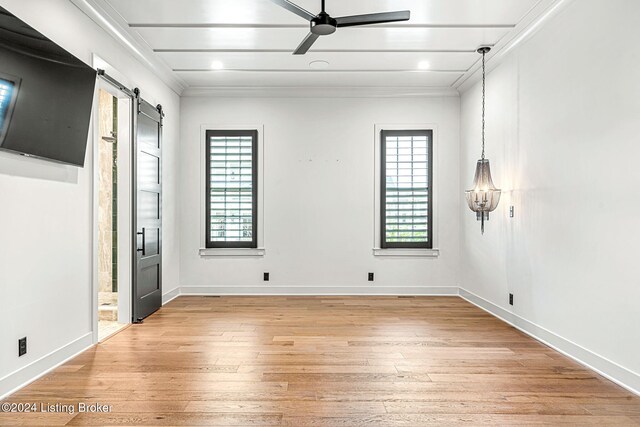 empty room with a barn door, a ceiling fan, baseboards, light wood finished floors, and crown molding