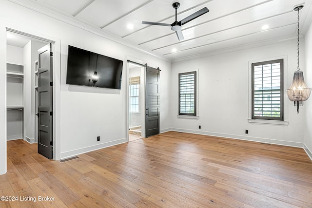 empty room with light wood-style floors, a barn door, and ceiling fan