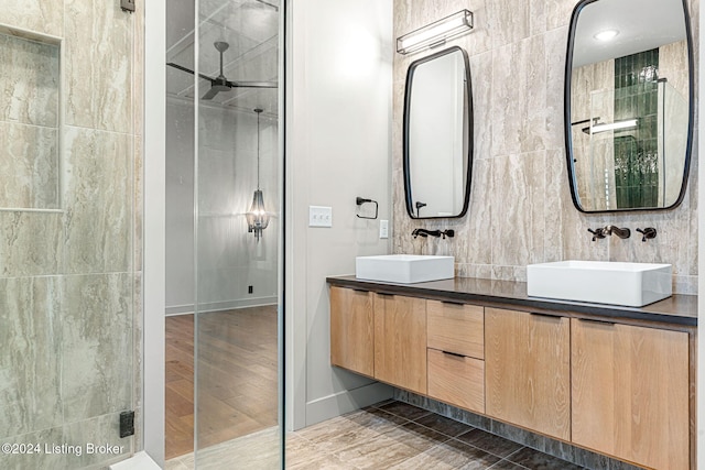 full bathroom with double vanity, a stall shower, a sink, and tile walls