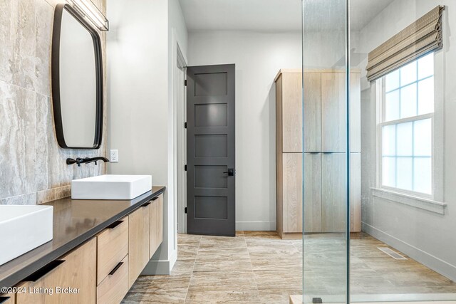 bathroom with double vanity, baseboards, visible vents, a walk in shower, and a sink