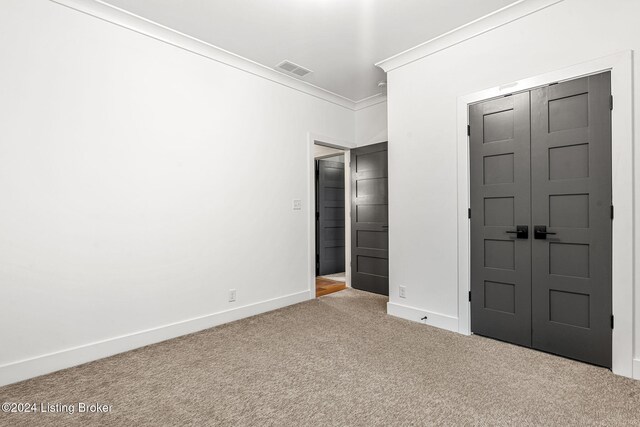 unfurnished bedroom with carpet flooring, visible vents, baseboards, ornamental molding, and a closet