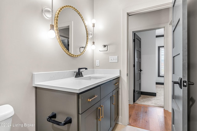 bathroom with toilet, wood finished floors, vanity, and baseboards