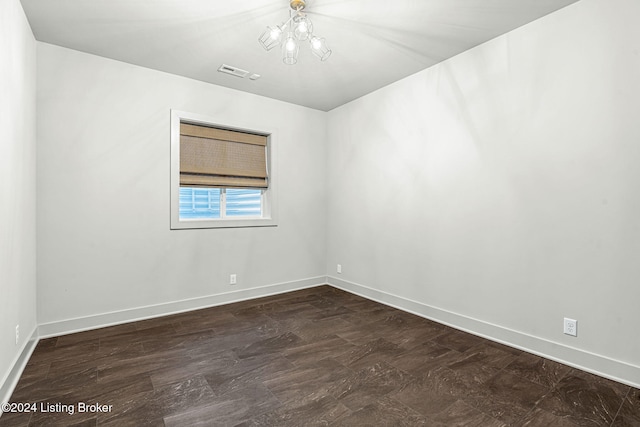 empty room with dark wood-type flooring, a chandelier, visible vents, and baseboards