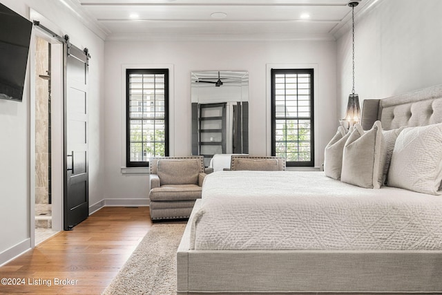 bedroom featuring ensuite bathroom, a barn door, wood finished floors, baseboards, and ornamental molding