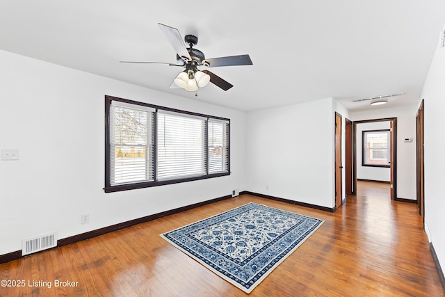 unfurnished room with a ceiling fan, visible vents, baseboards, and wood finished floors