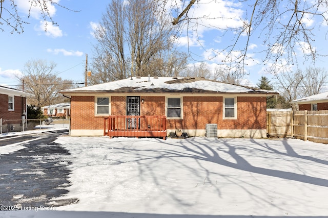 snow covered house with brick siding, fence, and central air condition unit