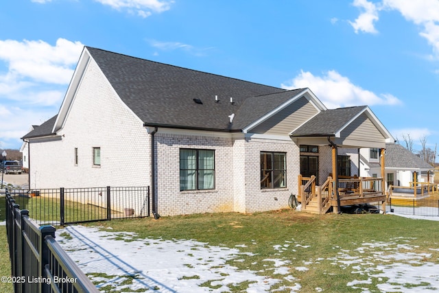 snow covered rear of property featuring a shingled roof, a lawn, fence private yard, a wooden deck, and brick siding