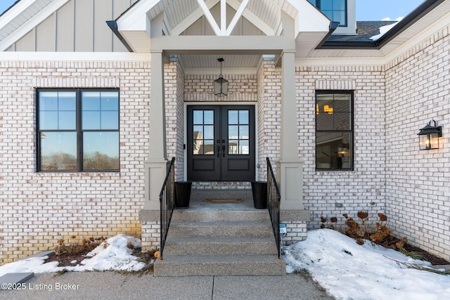 snow covered property entrance featuring french doors and board and batten siding