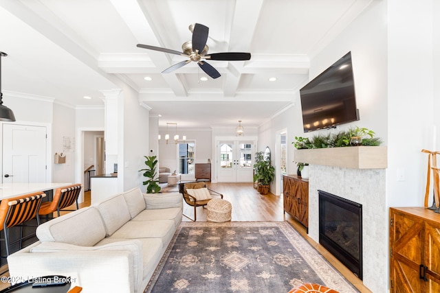 living area with coffered ceiling, ornamental molding, light wood-type flooring, beam ceiling, and a tiled fireplace