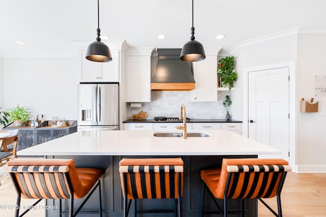 kitchen with a kitchen island with sink, a sink, white cabinets, custom exhaust hood, and stainless steel fridge