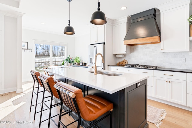 kitchen featuring a center island with sink, appliances with stainless steel finishes, custom exhaust hood, pendant lighting, and a sink