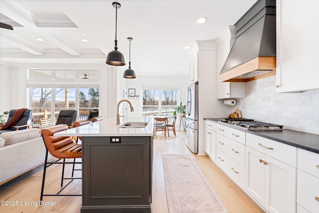 kitchen featuring dark countertops, premium range hood, a sink, and white cabinetry