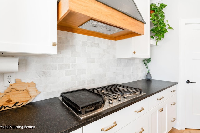 kitchen with stainless steel gas cooktop, tasteful backsplash, dark countertops, and white cabinets