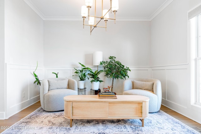 living area featuring a wainscoted wall, visible vents, ornamental molding, wood finished floors, and a chandelier