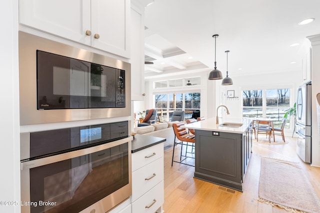 kitchen featuring a kitchen island with sink, stainless steel appliances, a sink, white cabinetry, and decorative light fixtures