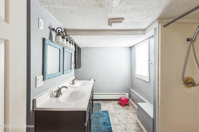 full bath with double vanity, a textured ceiling, a baseboard heating unit, and a sink