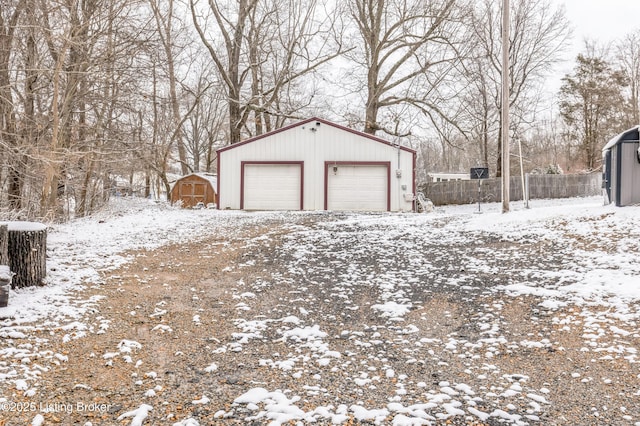 snow covered garage featuring a garage, fence, and a storage shed