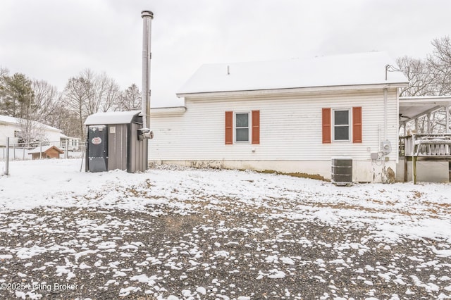 snow covered back of property with a carport and cooling unit