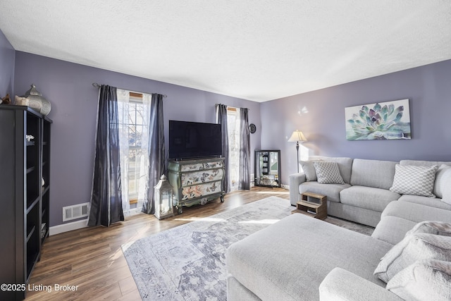 living room featuring visible vents, a textured ceiling, baseboards, and wood finished floors