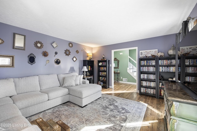 living room featuring dark wood-style flooring, visible vents, baseboards, and stairs