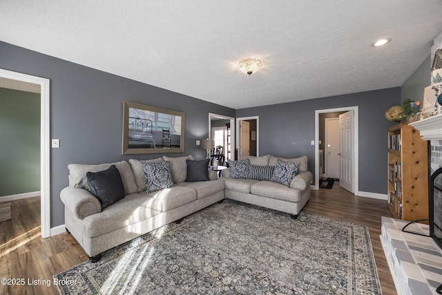 living room featuring a fireplace with raised hearth, a textured ceiling, baseboards, and wood finished floors