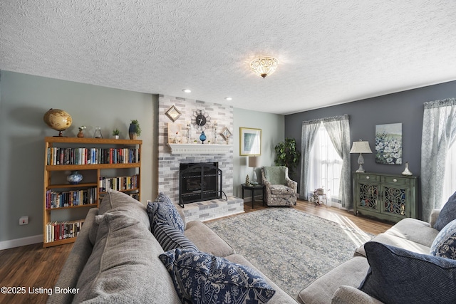 living room featuring a brick fireplace, a textured ceiling, baseboards, and wood finished floors