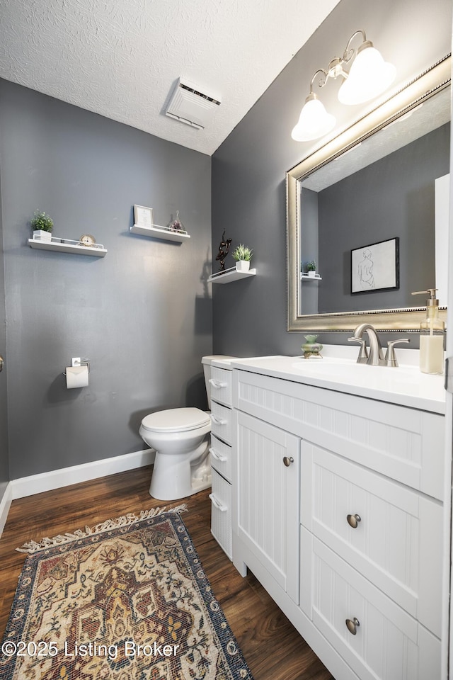 bathroom featuring baseboards, toilet, wood finished floors, a textured ceiling, and vanity