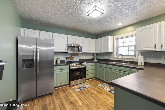 kitchen featuring white cabinets, dark countertops, an ornate ceiling, appliances with stainless steel finishes, and a sink