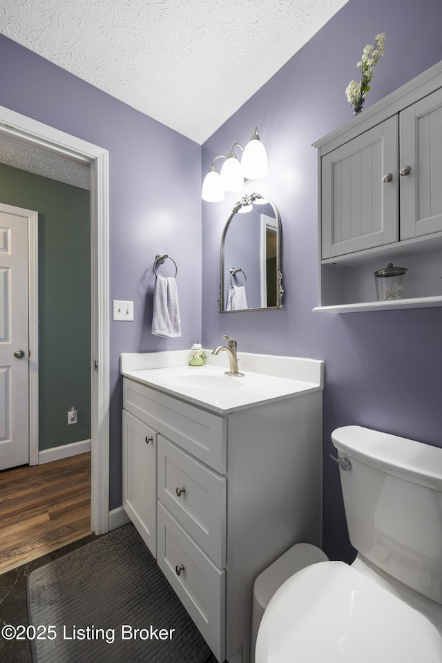 half bathroom featuring toilet, a textured ceiling, vanity, wood finished floors, and baseboards