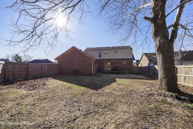 back of house with brick siding, a lawn, and a fenced backyard