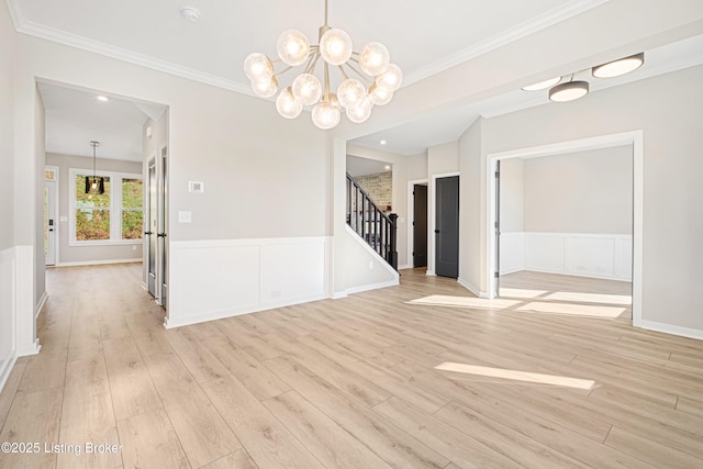 unfurnished room featuring a wainscoted wall, light wood-style flooring, stairway, and ornamental molding