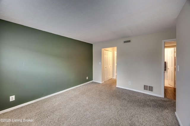 carpeted spare room featuring baseboards, visible vents, and a textured ceiling