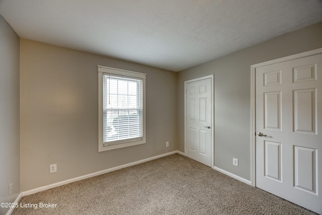 unfurnished bedroom featuring light colored carpet, a textured ceiling, and baseboards