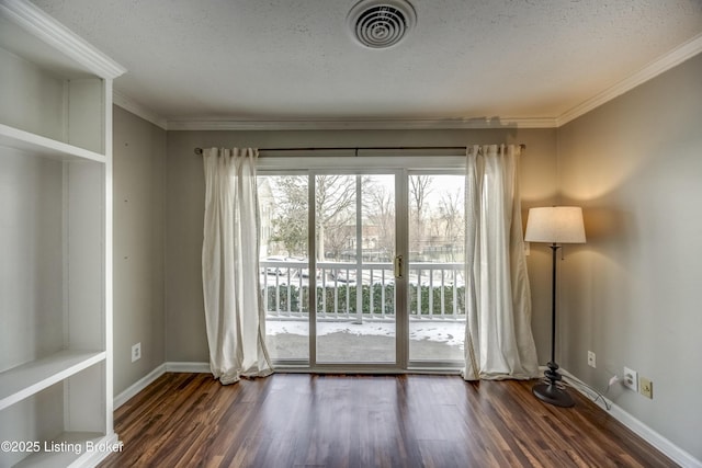 empty room with dark wood-type flooring, visible vents, crown molding, and baseboards